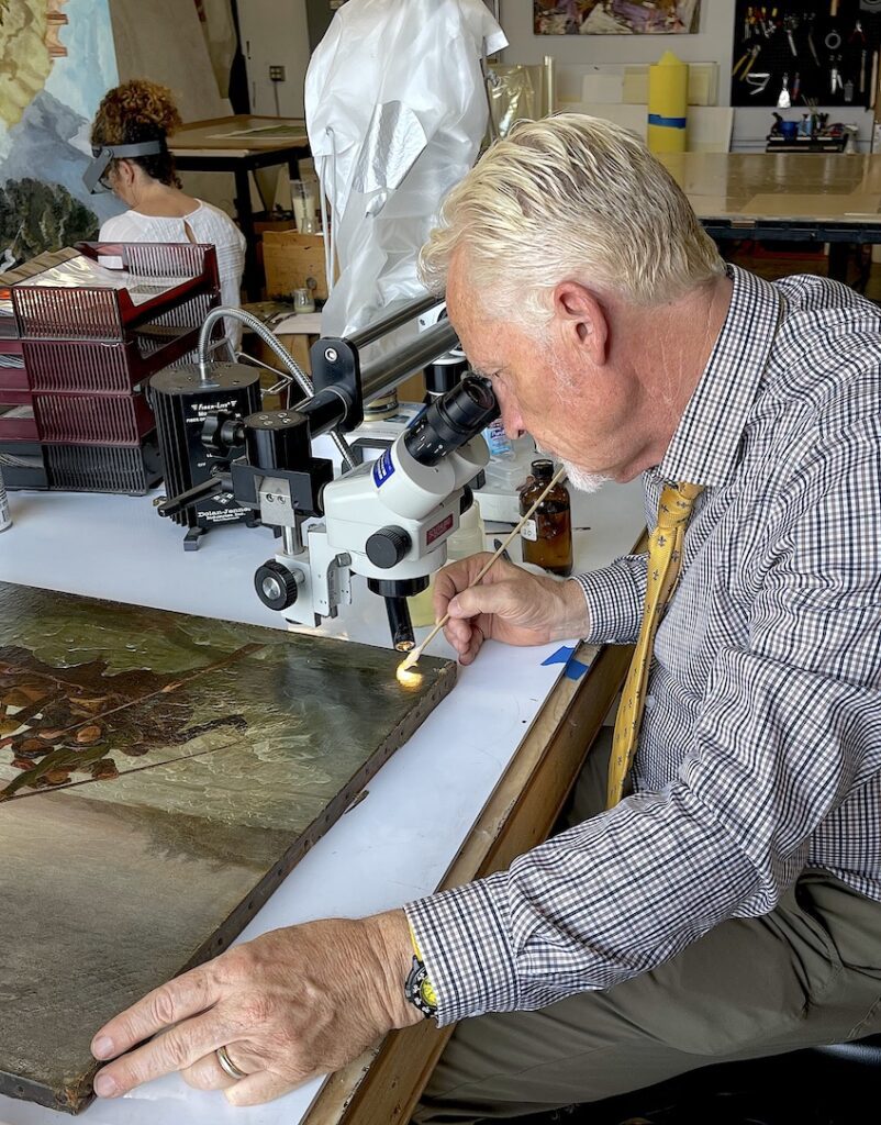 a white man looks into a microscope to evaluate a painting's condition for an art insurance claim