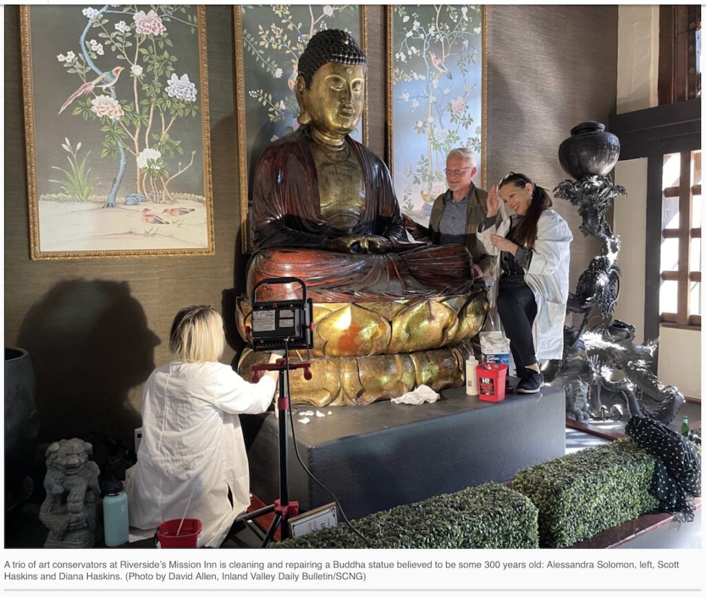 three people in lab coats evaluate and treat a large statue of a seated Buddha for an art insurance claim