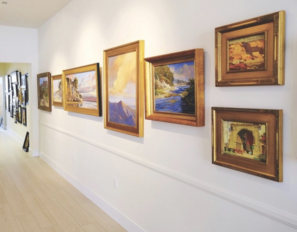 image of a white gallery wall with a row of framed paintings hung upon it