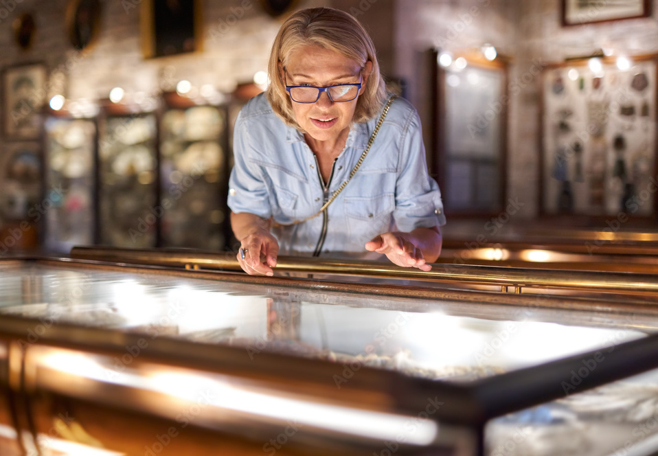 blonde woman leans over a glass case in a museum
