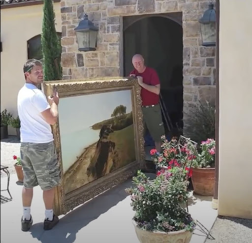 two men carrying a large painting with an ornate frame around it. It's important to pick a frame that can support the painting's weight and shape.
